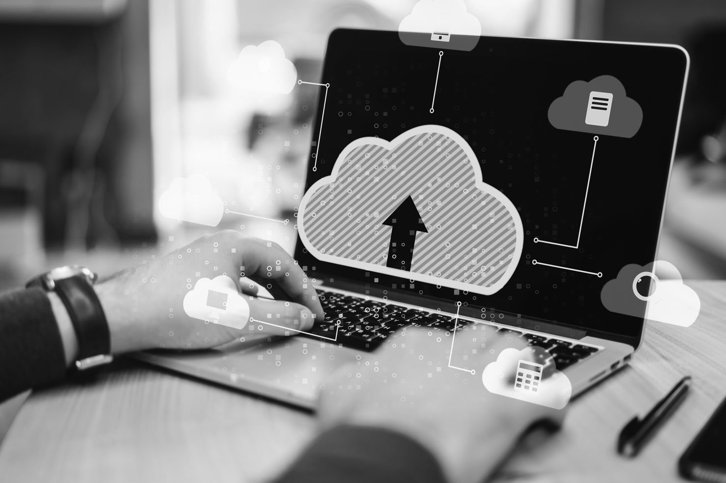 Hands typing on a laptop with cloud icons and an upload arrow on screen, symbolizing cloud computing. Monochrome setting.